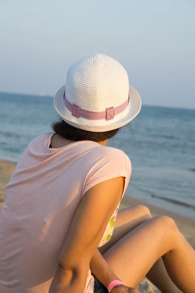 Fille brune en chapeau blanc regardant la mer tout en étant assis sur la plage — Photo