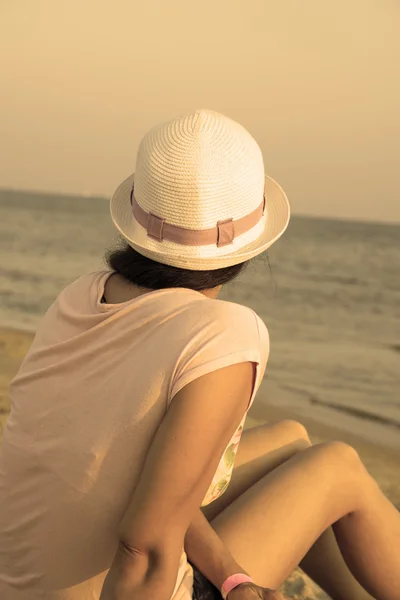 Fille brune en chapeau blanc regardant la mer tout en étant assis sur la plage chaud filtré — Photo