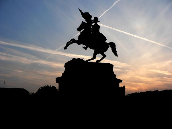 Black silhouette of monument of horse rider with flag on background of rose sunset