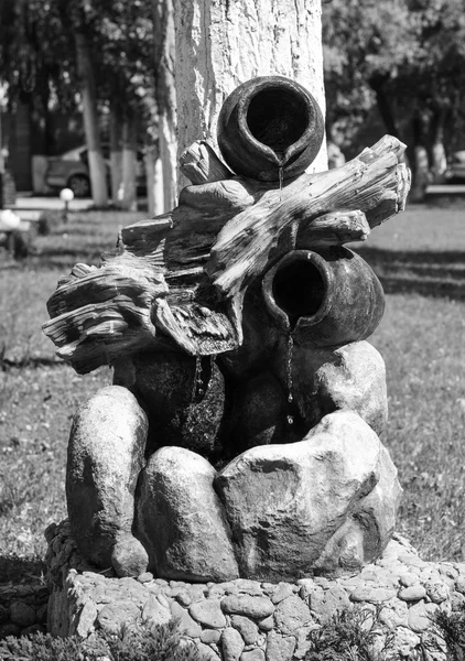 Декоративный фонтан из камней, горшков и куска дерева в парке черно-белый — стоковое фото