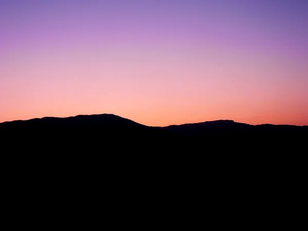 Silueta negra de las montañas sobre el fondo de la puesta de sol rosa — Foto de Stock