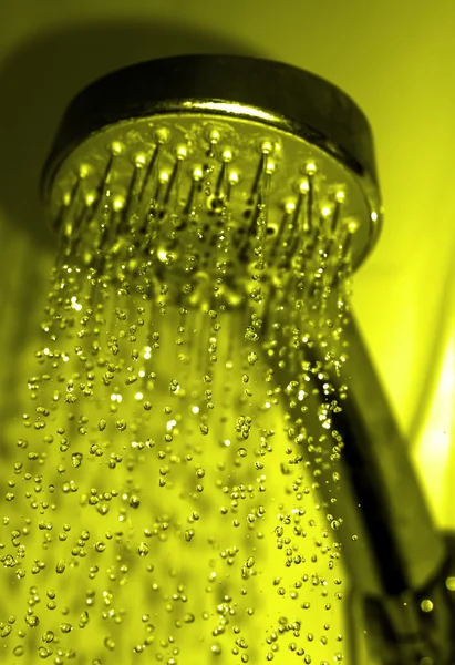 Waterdruppels close-up druipend uit de douche gele gefilterd — Stockfoto