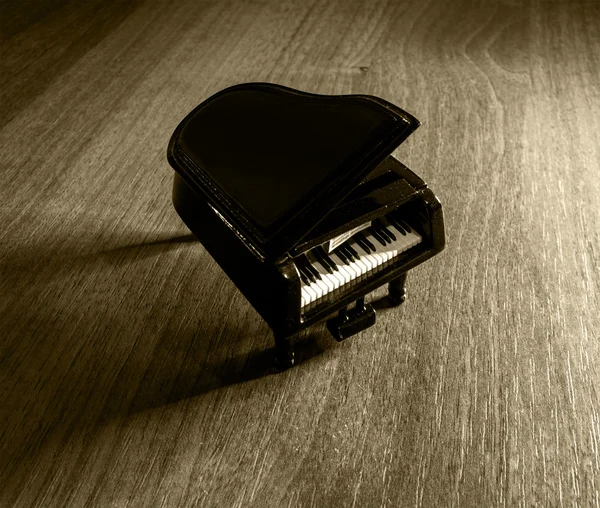 Modello in miniatura di pianoforte a coda nero con ombra su tavolo in legno filtrato — Foto Stock