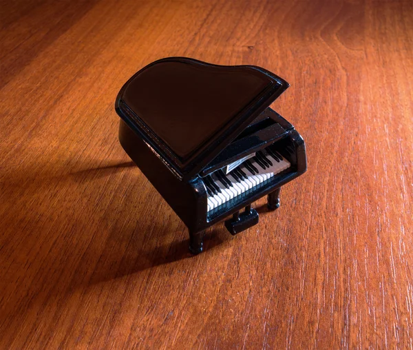 Modelo miniatura de piano de cola negro con sombra sobre mesa de madera roja — Foto de Stock