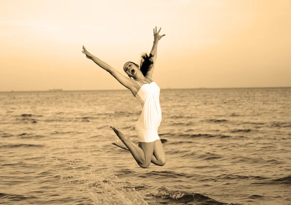 Ευτυχισμένος κορίτσι μελαχρινή άλμα πάνω από τη θάλασσα. Τυποποιημένος ως ρετρό φωτογραφία ζεστό φιλτραρισμένο — Φωτογραφία Αρχείου