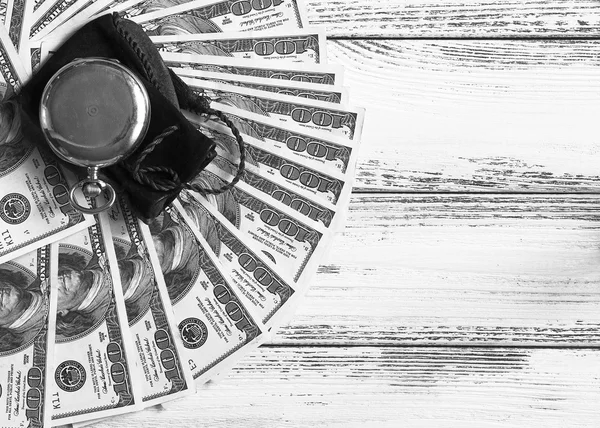 Pilha de dinheiro dólares dispostos como um ventilador com relógio de ouro antigo no fundo de madeira retro branco estilizado preto e branco — Fotografia de Stock