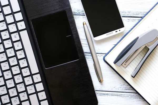 Lieu de travail moderne avec ordinateur portable, stylo argenté, smartphone, bloc-notes et agrafeuse sur table vintage en bois blanc — Photo