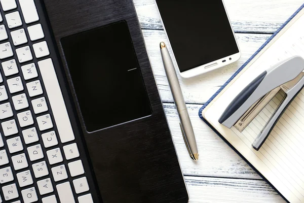 Lieu de travail moderne avec ordinateur portable, stylo argenté, smartphone, bloc-notes et agrafeuse sur table vintage en bois blanc chaud filtré — Photo