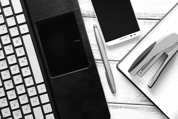 Lieu de travail moderne avec ordinateur portable, stylo argenté, smartphone, bloc-notes et agrafeuse sur table vintage en bois blanc noir et blanc — Photo