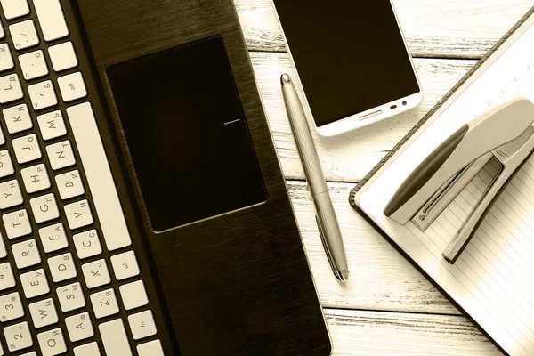Lieu de travail moderne avec ordinateur portable, stylo argenté, smartphone, bloc-notes et agrafeuse sur table vintage en bois blanc rétro filtré — Photo