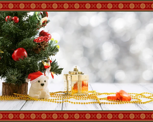 Greeting card with Christmas tree, gold gift box, balls, toy bear, candies and decorations on retro vintage white table isolated on white with red and golden ornament on blurred background — Stock Photo, Image