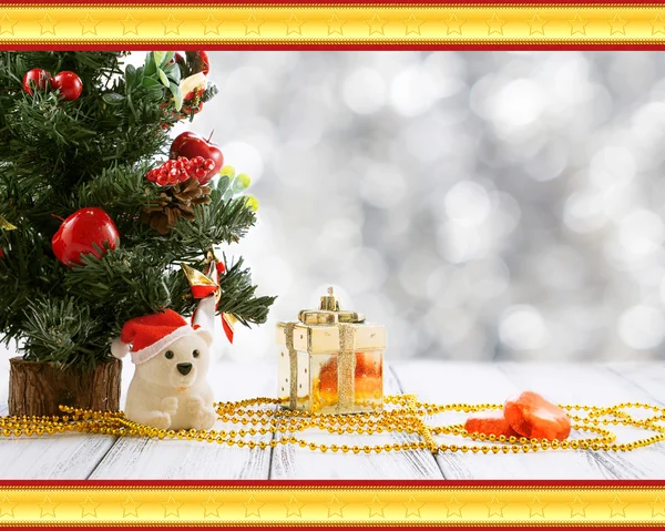 Greeting card with Christmas tree, gold gift box, balls, toy bear, candies and decorations on retro vintage white table isolated on white with red and golden ornament on blurred background — Stock Photo, Image