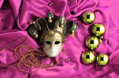 Background of golden Christmas tree balls with gold decorations and golden mask on pink shiny silk fabric with dramatic light and shadow