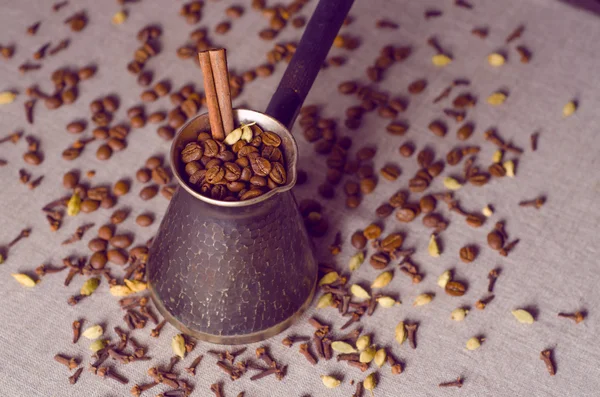 Turkish coffee pot filled with coffee beans and cinnamon stick on canvas background with spices scattered on it, vintage filtered — Stock Photo, Image