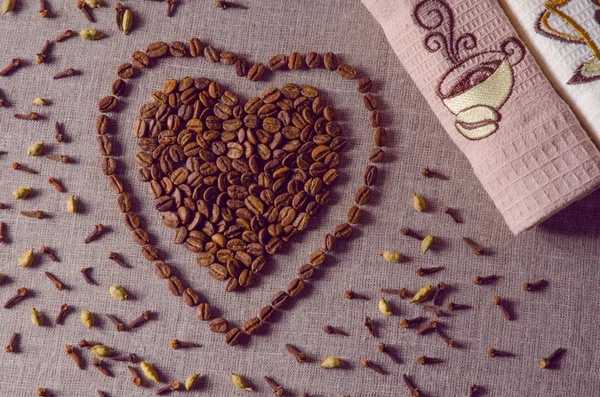 Кофейные зерна в форме сердца на фоне холста со специями, разбросанными по нему, полотенце, винтажные фильтруемые — стоковое фото