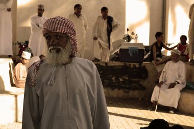 Older Omani man looks at the camera in an old outdoor marketplace in Oman.