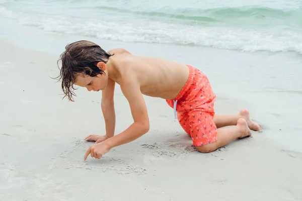 子供は熱帯のビーチで遊ぶ 子供は夏休みに海で遊ぶ 子供たちはビーチリゾートで楽しんでいます 面白い少年は砂の上に書き込みます アクティブ子供のライフスタイル 水泳の人々 — ストック写真