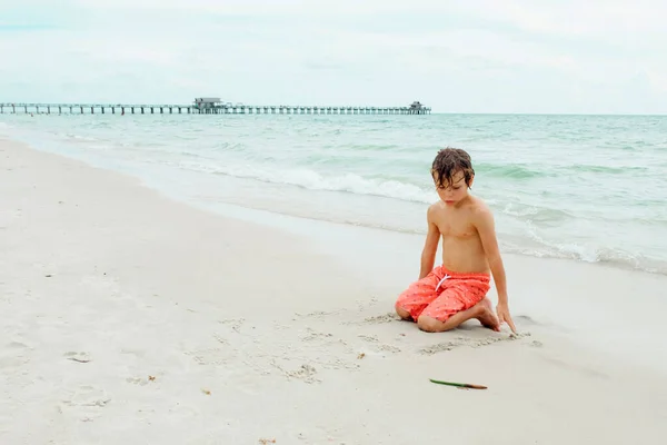 子供は熱帯のビーチで遊ぶ 子供は夏休みに海で遊ぶ 子供たちはビーチリゾートで楽しんでいます 面白い少年は砂の上に書き込みます アクティブ子供のライフスタイル 水泳の人々 — ストック写真