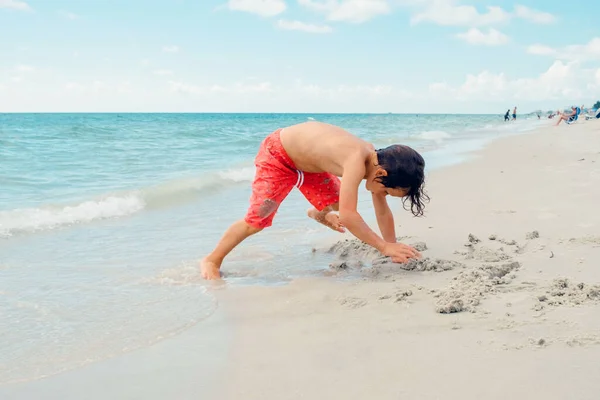 子供は熱帯のビーチで遊ぶ 子供は夏休みに海で遊ぶ 子供たちはビーチリゾートで楽しんでいます 面白い少年は砂の上に書き込みます アクティブ子供のライフスタイル 水泳の人々 — ストック写真