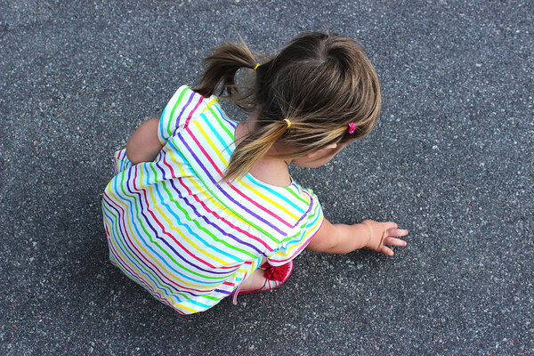 Маленькая девочка сидит на асфальте
