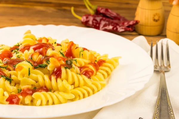 Italian pasta fusilli with tomato sauce in plate, napkin and fork on wooden table — Zdjęcie stockowe