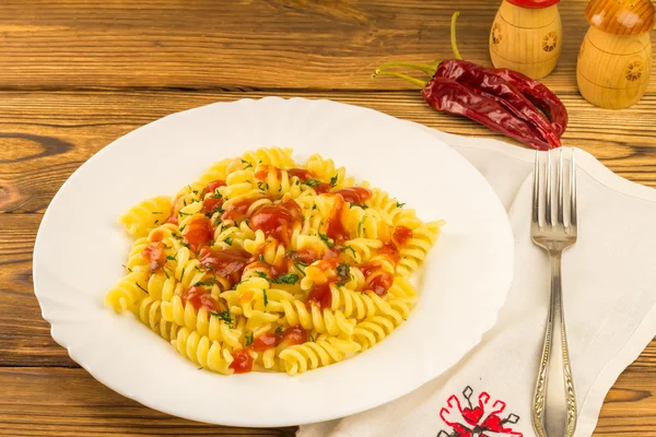 Italian pasta fusilli with tomato sauce in plate, napkin and fork on wooden table — Stock Photo, Image