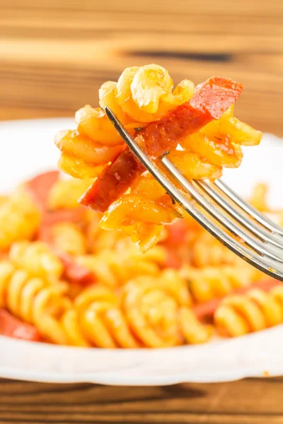 Italian pasta fusilli with tomato sauce and sausage skewered on fork in plate, close-up, selective focus — Zdjęcie stockowe