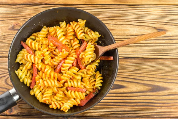 Italian pasta fusilli with tomato sauce and sausage in pan, wooden spoon on table, top view, space for text — Zdjęcie stockowe