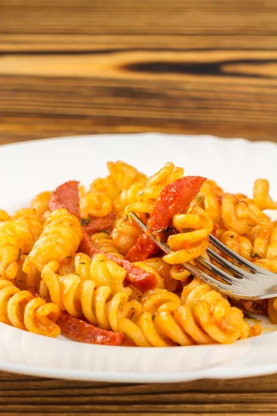 Italian pasta fusilli with tomato sauce and sausage skewered on fork in plate, close-up, selective focus — Zdjęcie stockowe