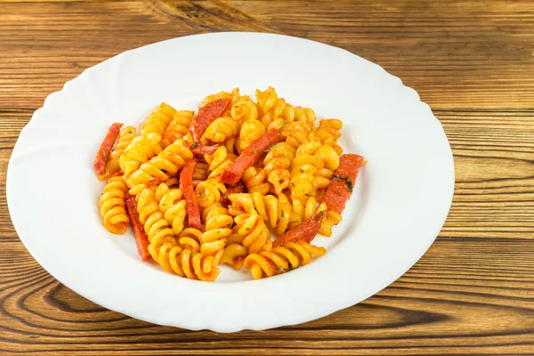 Italian pasta fusilli with tomato sauce and sausage in plate on wooden table — Zdjęcie stockowe