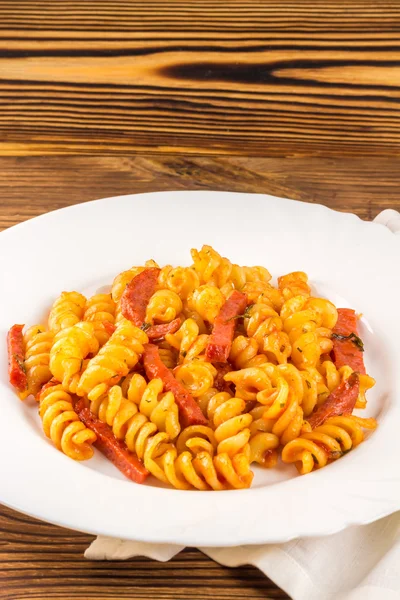Italian pasta fusilli with tomato sauce and sausage in plate, napkin on wooden table — Zdjęcie stockowe