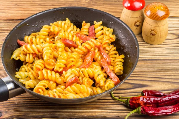 Italian pasta fusilli with tomato sauce and sausage in pan, red pepper on wooden table, space for text — Zdjęcie stockowe
