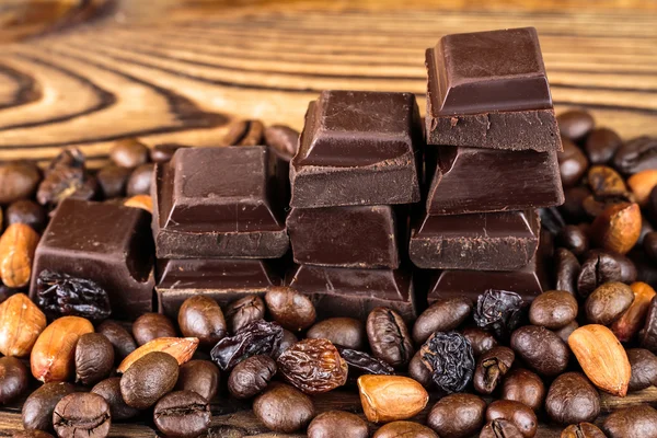 Dark chocolate cubes, coffee beans, peanuts and raisins on wooden table, close-up — Stock Photo, Image