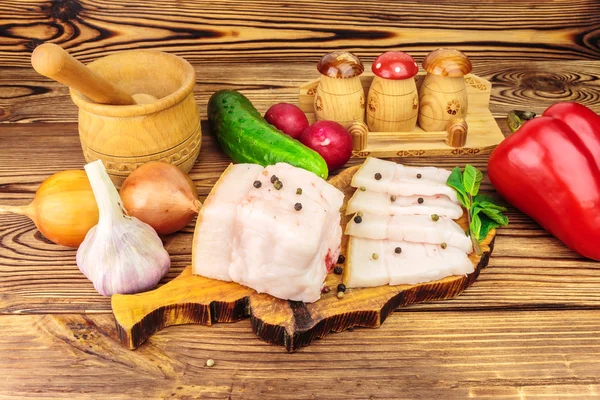 Trozos y rebanadas de manteca de cerdo fresca y cruda sobre tabla de madera con verduras, especias sobre la mesa . — Foto de Stock