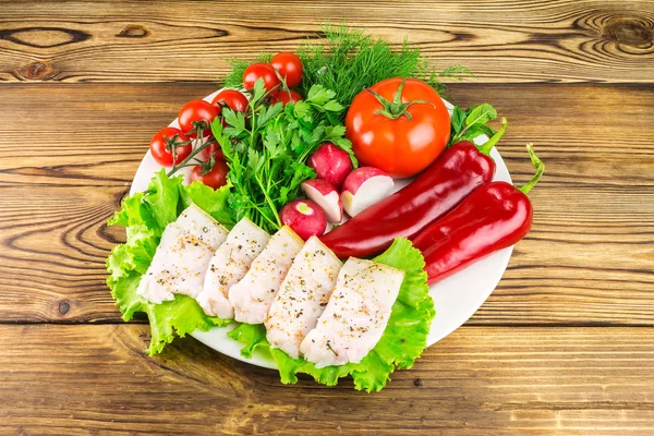 Тарілка з нарізаним свіжим свинячим салатом, свіжими продуктами, овочами на дерев'яному столі . — стокове фото