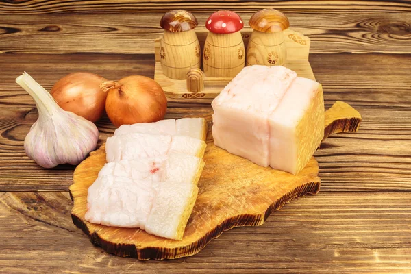 Piece and sliced fresh, raw pork lard on wooden board, garlic, onion on the table. — Stock Image Piece and sliced fresh, raw pork lard on wooden board, garlic, onion on the table. Royalty Free Stock Photos