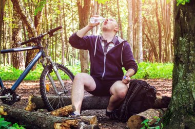 Sırt çantası ile Bisikletçi, genç adam şişeden su içme, güzel ormanda, yaz yolculuğu.