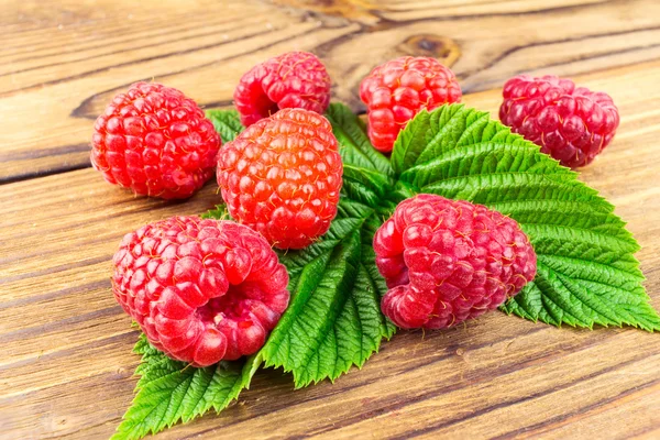 Fresh, ripe raspberries on leaves, rustic wooden background. — Stock Photo, Image