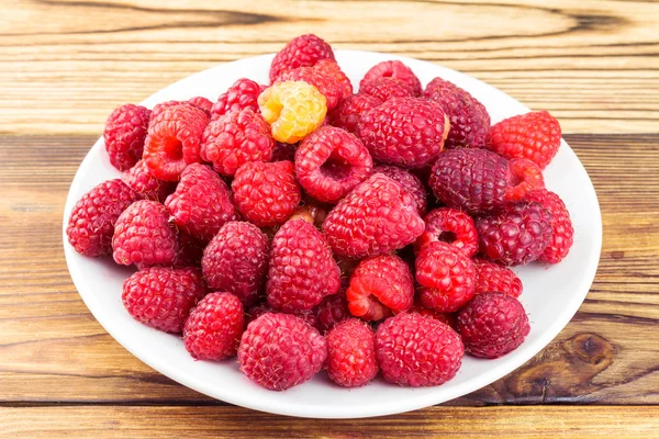 Plate full of ripe raspberries on rustic wooden table. — Stock Photo, Image