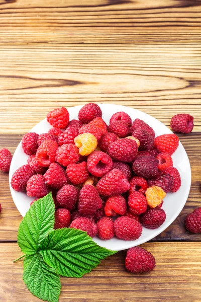 Plate full of ripe raspberries on rustic wooden table. — Stock Photo, Image