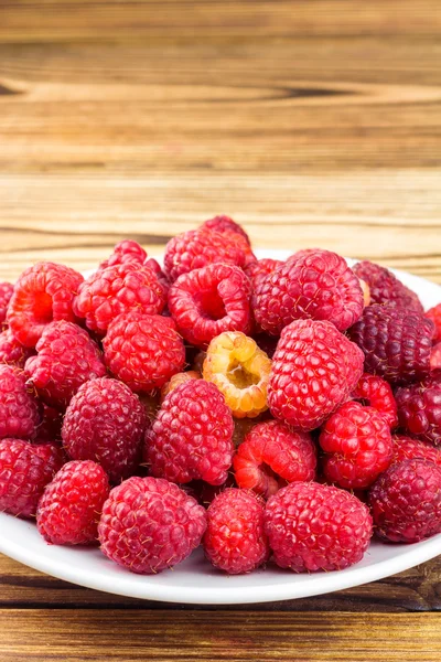 Plate full of ripe raspberries on rustic wooden table. — Stock Photo, Image