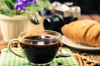 Kruvasan, vintage fotoğraf makinesi, saksıyı, kafede ahşap masa ile yeşil peçete üzerinde siyah kahve fincan. seyahat kavramı