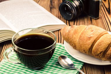 Peçete kruvasan, açık kitap, vintage fotoğraf makinesi, ahşap masa, seyahat kavramı üzerinde siyah kahve