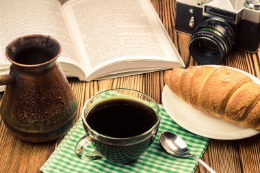 Kruvasan, açık kitap, Türk cezve, vintage fotoğraf makinesi, ahşap masa peçete üzerinde siyah kahve
