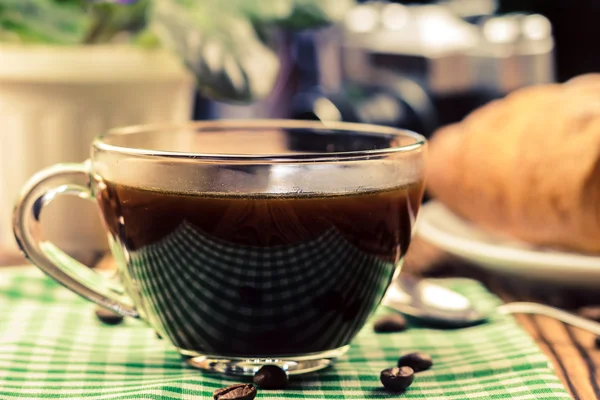 Tasse de café noir sur serviette verte avec croissant, appareil photo vintage, pot de fleurs, table en bois dans le café. concept de voyage — Photo
