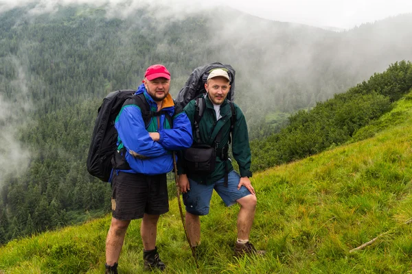 Portrait of two man hikers with backpacks in Carpathian mountains, summertime journey