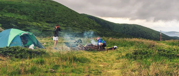 Tienda de campaña y dos hombres turistas en fogata en las montañas de los Cárpatos, viaje de verano . — Foto de Stock