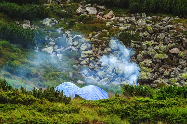 Camping tent and campfire smoke in Carpathian mountains, summertime journey.