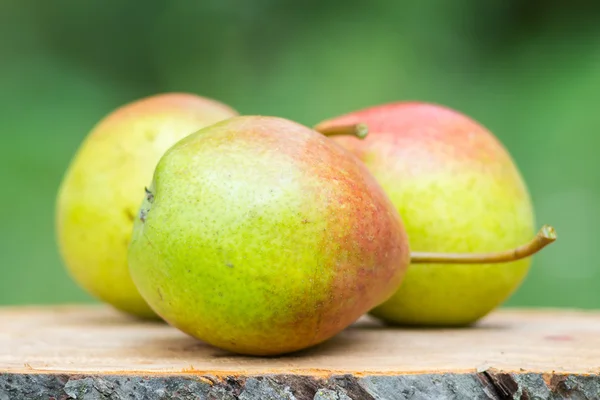 Three ripe organic pears on wooden board, blurred background, selective focus. — Stock Photo, Image