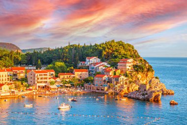 Budva Riviera 'daki Adriyatik sahil manzarası. Günbatımında kayaların üzerinde binaları olan Przno köyü Karadağ 'ın sıcak güneş ışığı altında.